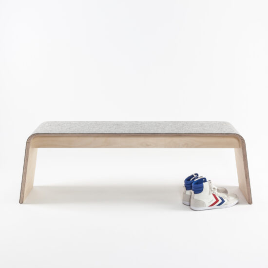 die sitzbank von stadig aus hellem holz und hellgrauem filzbezug unter der ein paar turnschuhe steht
