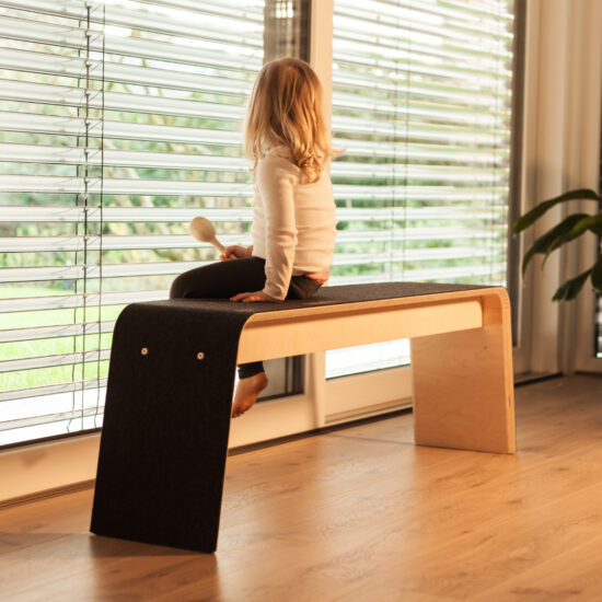 ein kleines mädchen mit blonden haaren sitzt auf der bank von stadig aus hellem holz und dunklem filzbezug