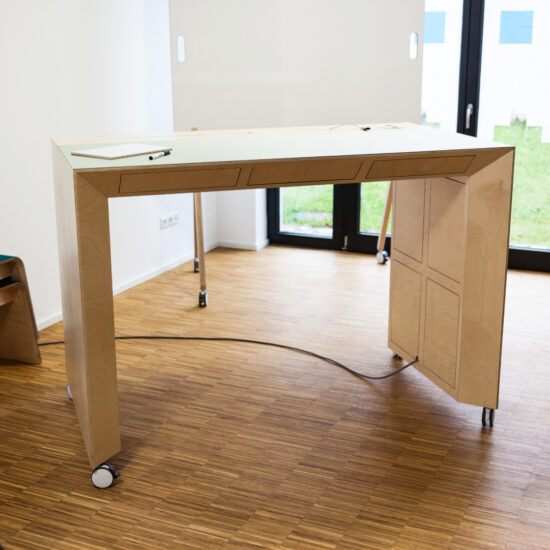 der pop up raum von moveable.space mit einem hohen arbeitstisch aus holz und dahinter ein whiteboard vor einem fenster