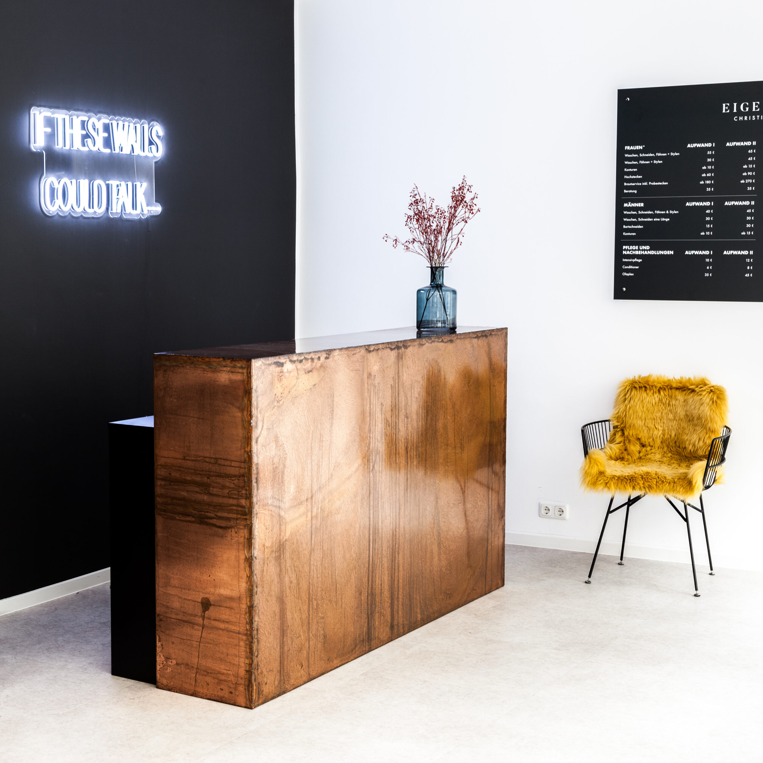 moderner empfangsbereich mit metallenem tresen und schwarzer wand dahinter ein neonschriftzug