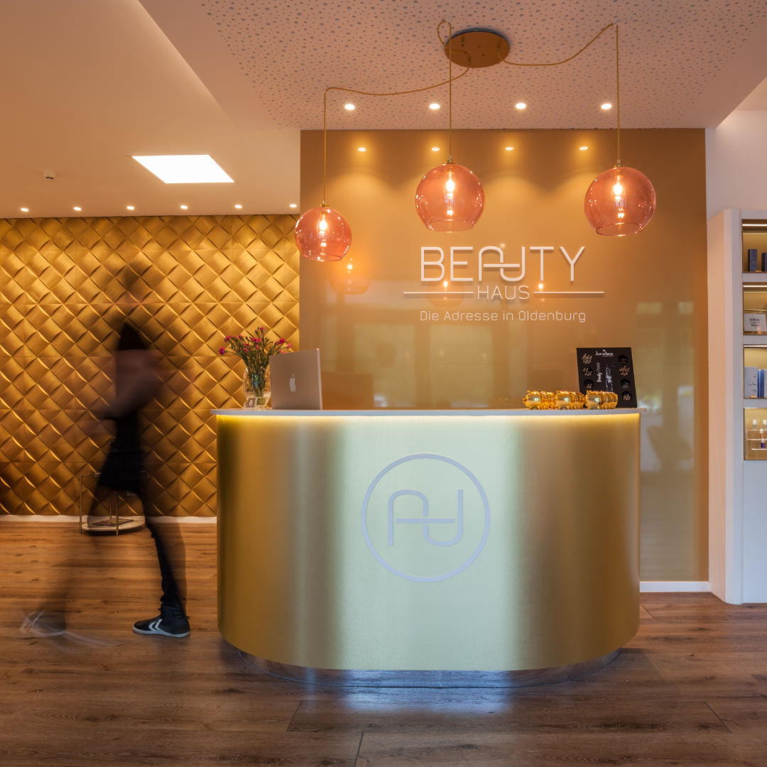 moderner empfangsbereich mit goldenem tresen, warmer beleuchtung und beauty-studio-logo